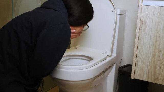 Young woman feeling sick and vomiting into a toilet in the bathroom, representing illness, nausea, discomfort, and a moment of physical distress at home.