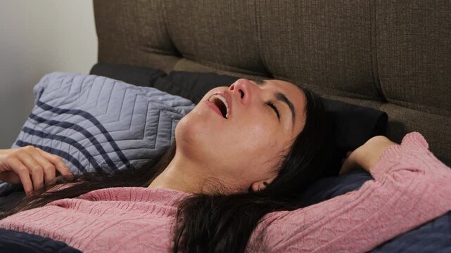 Young woman lying on her back in bed, covered with a blanket, sleeping deeply and snoring, representing natural sleep, relaxation, rest, and everyday nighttime comfort in a cozy bedroom at home.