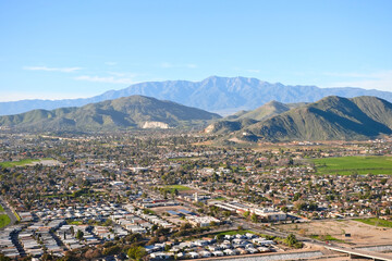 Panoramic aerial view of Riverside, California from Mount Rubidoux, showing suburban neighborhoods, green valley land, and surrounding mountains.