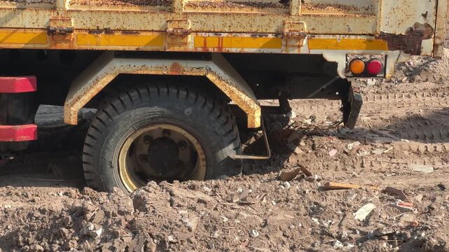 A dump truck wheel sinks into soft soil at a construction site, highlighting poor ground conditions and site access challenges.