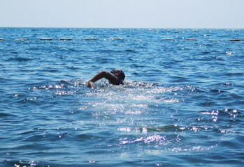 Wide-angle view of a young boy swimming freestyle in open blue sea on a sunny day, water splashing around him, conveying summer activity, fitness, freedom, and outdoor adventure.