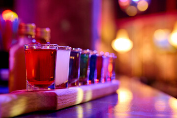 Colorful shot glasses arranged on a wooden tray in warm ambient lighting, creating a vibrant, festive scene ideal for nightlife, parties, bars, and cocktail promotions.