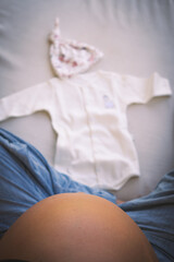 Mujer embarazada sentada con ropa de reci&eacute;n nacido, concepto de preparaci&oacute;n para el parto.