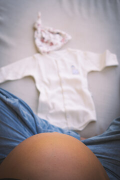 Mujer embarazada sentada con ropa de reci&eacute;n nacido, concepto de preparaci&oacute;n para el parto.
