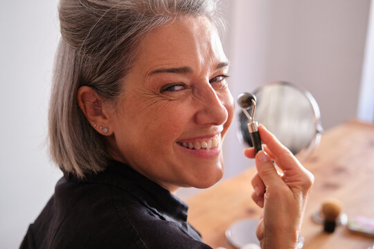 Happy mature woman holding a jade roller massager for face massage at home