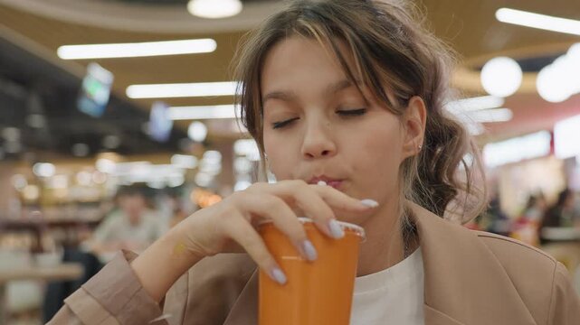 teen caucasian food reviewer tasting pizza and sipping drink in crowded food court, thoughtful tasting expression, ambient lights, orange cup on table, casual blazer, culinary focus, candid