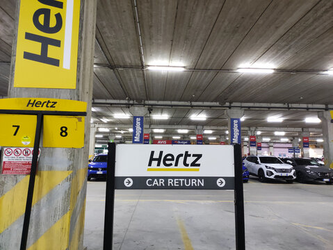 Cagliari, Italy - January 15, 2026: Hertz car return sign in a parking garage with visible vehicles and signage indicating rental services in Singapore location