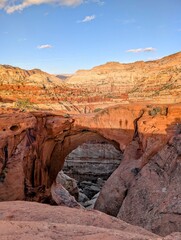 Majestic natural sandstone arch glowing in the warm golden light of the setting sun, showcasing the vastness of a rugged desert landscape with distant mountains