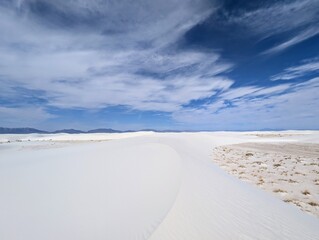 A serene and expansive desert landscape unfolds with pristine white sand dunes stretching into the distance under a brilliant blue sky dotted with wispy clouds © Martin