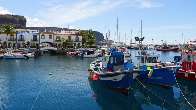 Puerto de Mogan, Gran Canaria &ndash; Marina with colorful-trimmed houses, palm trees, sailing boats and fishing boats under sunshine