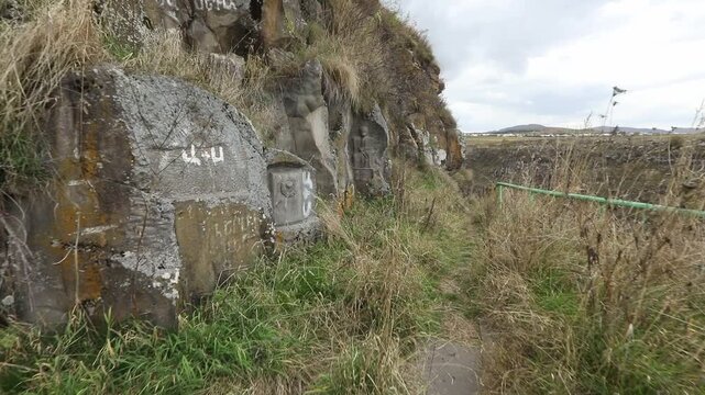 A rock wall featuring carved Soviet-era memorials. The shot moves past a carved USSR emblem to reveal a larger bas-relief of historical figures carved directly into the natural cliff face.

