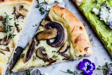 Four slices of rustic wild pizza topped with mushrooms and herbs are placed on a wooden table. Fresh ingredients create a simple meal