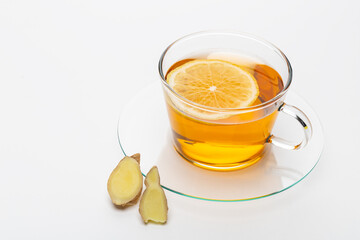 Ginger tea with lemon slice on a glass plate with fresh ginger pieces nearby