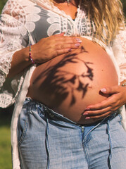 Primer plano de mujer embarazada y su pareja sosteniendo el vientre al aire libre bajo la luz del sol.