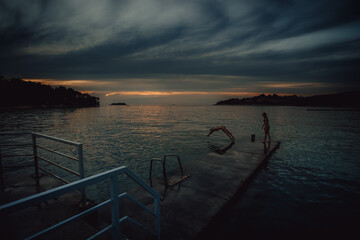 Obraz premium Insel Kovarsada - In der Abenddämmerung springt ein Mädchen von einem Steg aus mit einem Kopfsprung ins Wasser, Vrsar, Istrien, Kroatien