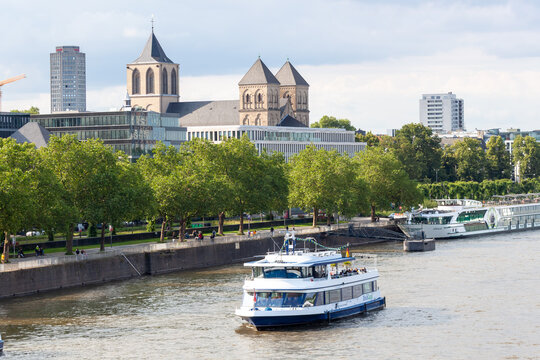 The white passenger ferry Rheingold cruising on the Rhine river in Cologne, Germany. Urban riverfront view with the historic St. Heribert church and modern buildings under a cloudy sky