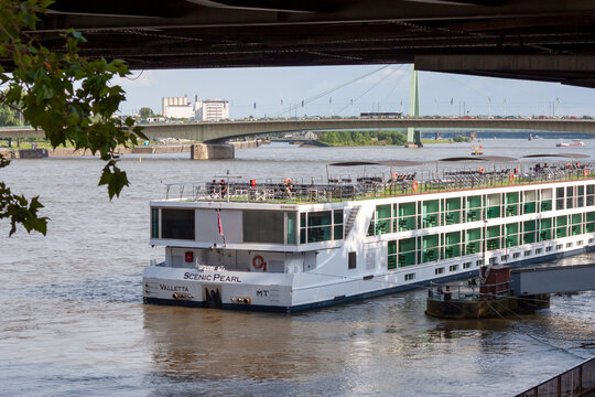 The luxury river cruise ship Scenic Pearl anchored on the Rhine river in Cologne, Germany. View of the vessel with the Severinsbrucke bridge and urban landscape in the background