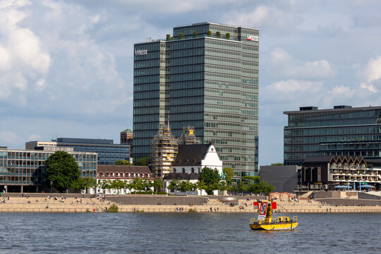 The modern glass facade of the Lanxess Tower skyscraper and the historic St. Heribert church on the banks of the Rhine river in Cologne, Germany. Urban riverfront with people on the stairs