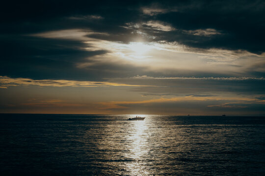 Stimmungsvolle Abendstimmung an der K&uuml;ste von Istrien in Kroatien: Ein Motorboot f&auml;hrt &uuml;ber das Meer vor dem Horizont, w&auml;hrend die Sonne untergeht, Istrien, Kroatien