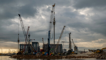 Obraz premium Construction cranes and machinery on coastal site with overcast sky.