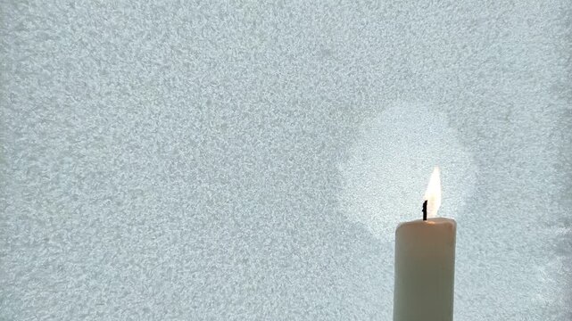 A candle burns against the background of iced glass