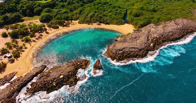 Turquoise water of the Atlantic hitting the rocks that protect beautiful beach. Approaching Mar Chiquita Beach in Manati, Puerto Rico surrounded by lush greenery.