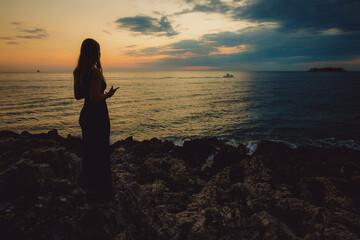 Silhouette einer jungen Frau mit langen Haaren, die im Abendrot am Strand von Istrien steht und auf das Meer schaut, Kroatien