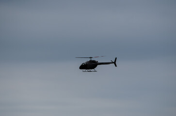 Single helicopter flying at an angle silhouetted against a pale blue sky