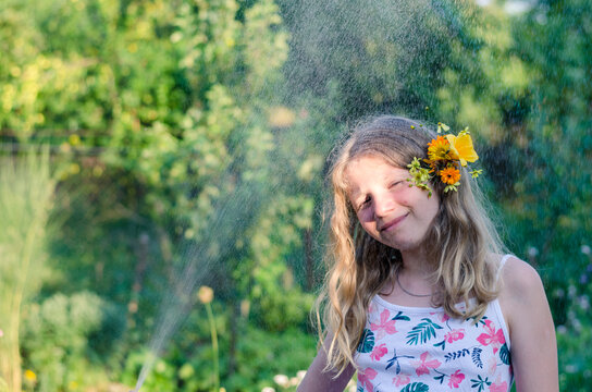 portrait of teenage girl with flowers in hair, having fun with spraying water
