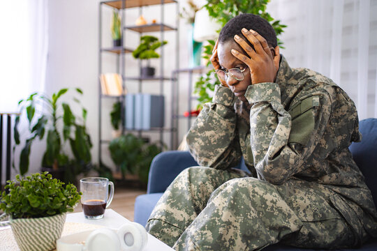 Depressed african american soldier suffering from ptsd sitting on sofa at home