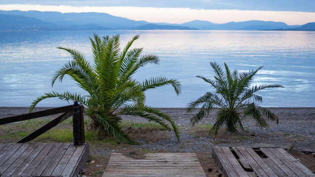 Empty outdoor cafe terrace with wicker chairs overlooking a calm sea bay and mountains at dusk. - Powered by Adobe