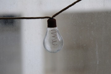 Incandescent light bulb hanging on a rope with blurred background.