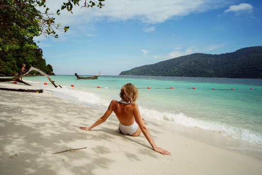 Mother and child relaxing on a sandy tropical beach and looking at the turquoise sea. Summer vacation, family travel and lifestyle concept. Calm, bonding, relaxation and quality time by the ocean.