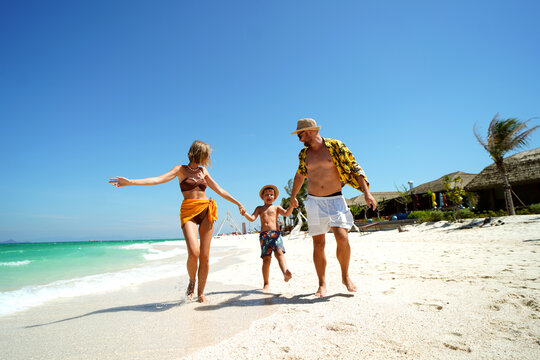 Happy family with a child holding hands and having fun on a beautiful tropical beach. Summer vacation, travel and lifestyle concept. 