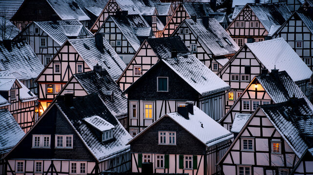 Snow covers rooftops in a village during winter evening, giving a cozy look to the scene