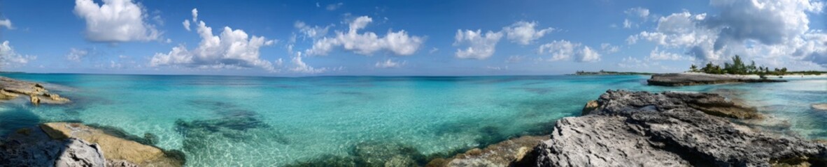 Fototapeta premium Panoramic ocean view with clear waters and rocky shoreline under blue sky
