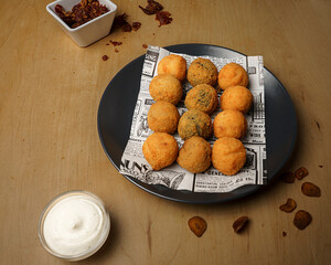 Top view of crispy fried croquettes on newspaper paper with dipping sauce and spices on wooden table