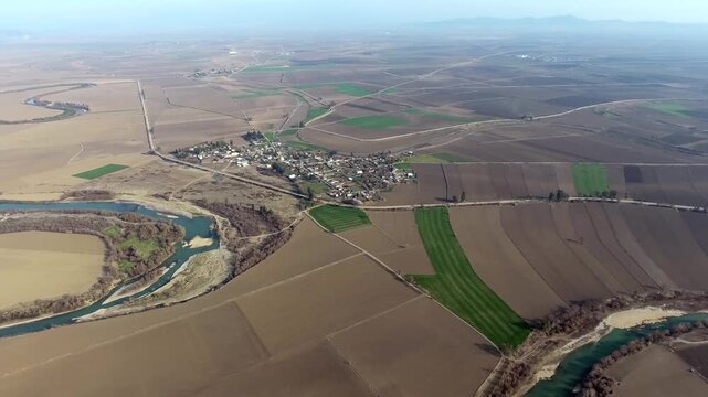 Aerial view of rural farmland and village houses across brown fields on flat Spanish plain. Wide landscape shows agricultural plots, small settlement and cultivated terrain in Castilla La Mancha Spain