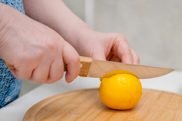 A woman's hands cut a lemon with a knife on a wooden board