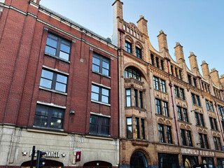 Naklejka premium Historic brick and stone building along Manchester street with shops and pedestrians in the UK