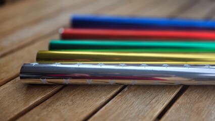 Colorful metallic wrapping paper rolls on wooden surface for gift packaging and crafting
