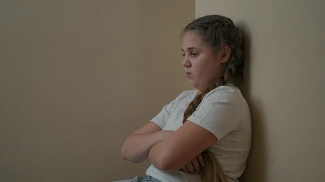 Upset girl sits near wall with arms crossed. Angry child shows frustration. Girl pouting with folded arms. Frustration builds as child stays upset. Rebellion seen in angry child body language