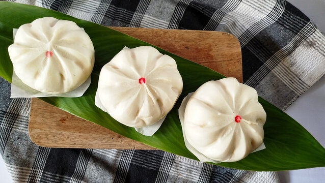 Steamed buns known as bao zi or bakpao served on banana leaf and wooden cutting board. Soft white buns with pleated tops and red dot detail for Asian food concepts.