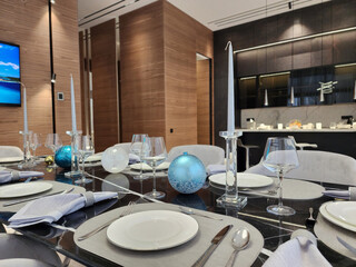 New Year's table setting in the interior of a spacious room. Glasses, candles, cutlery, Christmas...