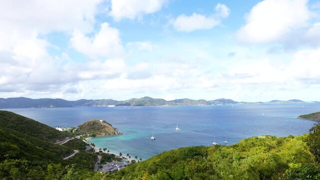 sailboats and catamarans and yachts sail the Caribbean Ocean through the British Virgin Islands in the wide shot of the sea's horizon from high up on an island
