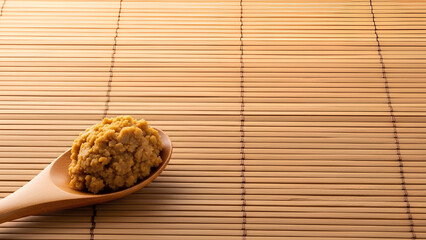 Traditional missô paste scooped onto a wooden spoon positioned in the lower left of a large smooth bamboo mat surface, extensive right and upper area kept empty as negative space for text.
