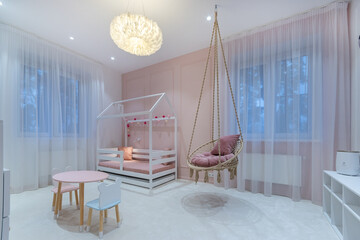 This kids room shows a modern design with a hanging chair, a low bed in a house shape, and a round...
