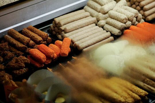 Assorted Dutch fried snacks in heated display case including bitterballen, frikandellen, and kroketten. Traditional Dutch fast food perfect for culinary, food service, and cultural cuisine content.