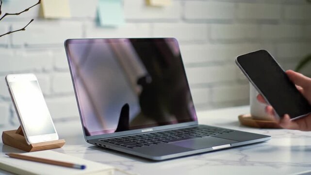 Dolly video of a professional hand in a white shirt typing on a silver laptop, a white smartphone, and minimalist tools on a marble desk in natural light. Concept of modern home office productivity