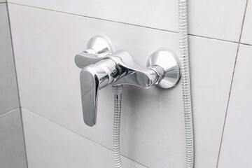 Modern chrome shower faucet mounted on tiled bathroom wall. Minimal bathroom plumbing fixture closeup. Wall mounted shower mixer tap with hose connection. Clean interior detail for home hygiene.